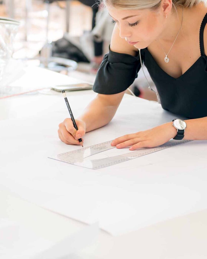 Schülerin arbeitet händisch an Schnittentwürfen